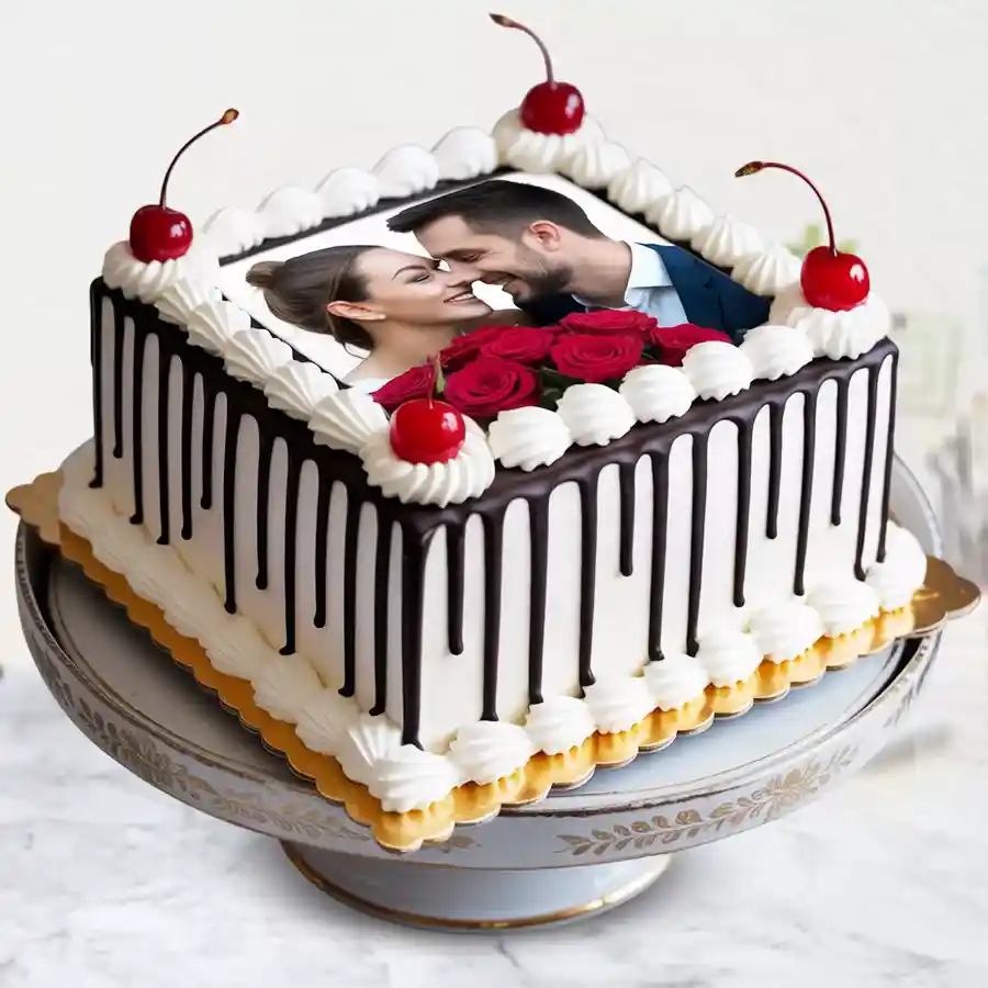 Square Black Forest photo cake decorated with white frosting, dark chocolate flakes, and fresh cherries, featuring a personalized photo on top.
