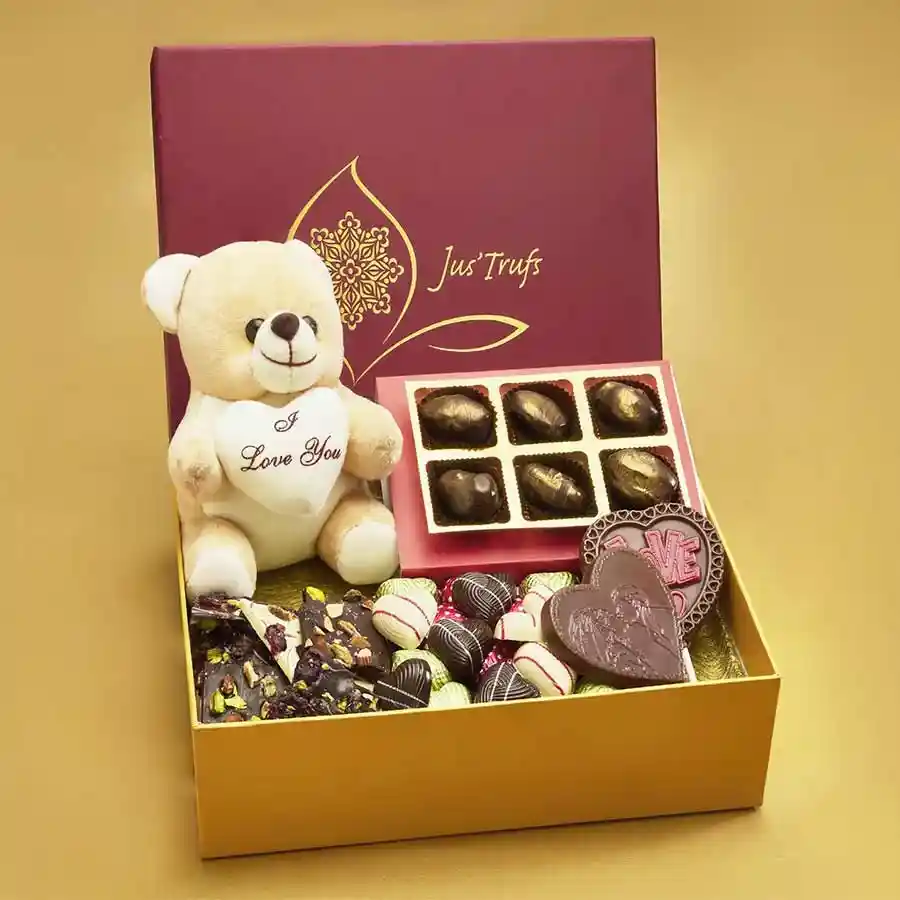 Cherished Moments Chocolate Gift featuring artisanal dark chocolate-coated dates, Belgian chocolate barks with cranberries and pistachios, heart-shaped milk chocolates in various flavors, lollipops, and a cuddly teddy bear.