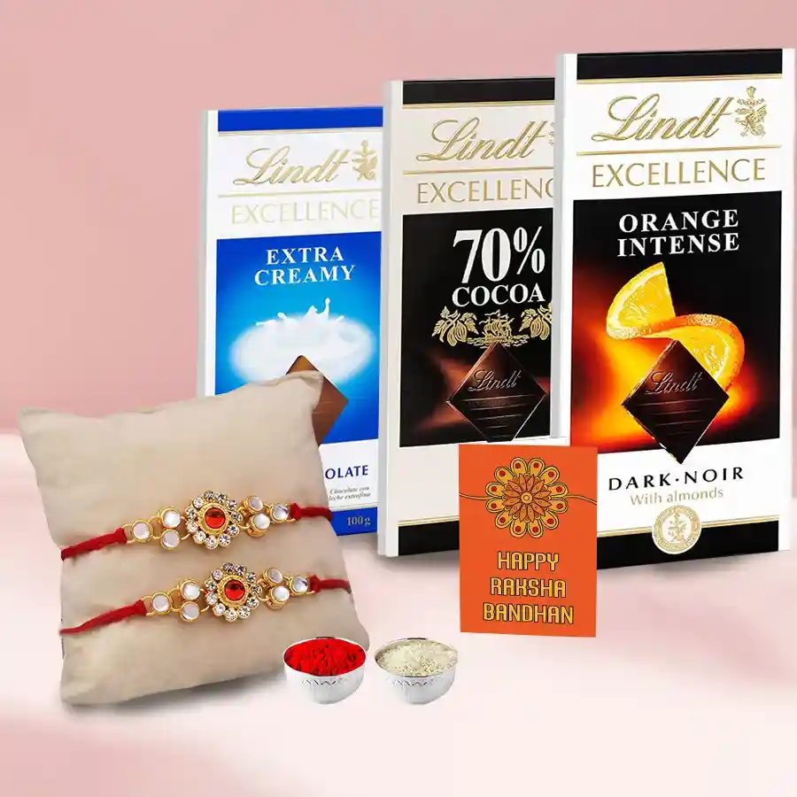 An assortment of Lindt chocolate bars including Extra Creamy, Orange Intense, and Excellence 70, alongside two Rakhis and Roli Tilak Chawal sets on a decorative background.