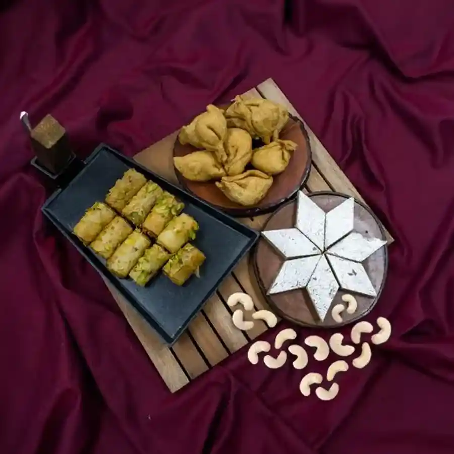 A beautifully arranged gift set featuring Haldiram Kaju Barfi, Dunkel Braun Roll Baklava, and Mini Samosas for a perfect celebration.