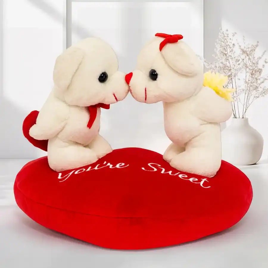 Love's Embrace Teddy on a heart-shaped cushion with a kissing couple design.