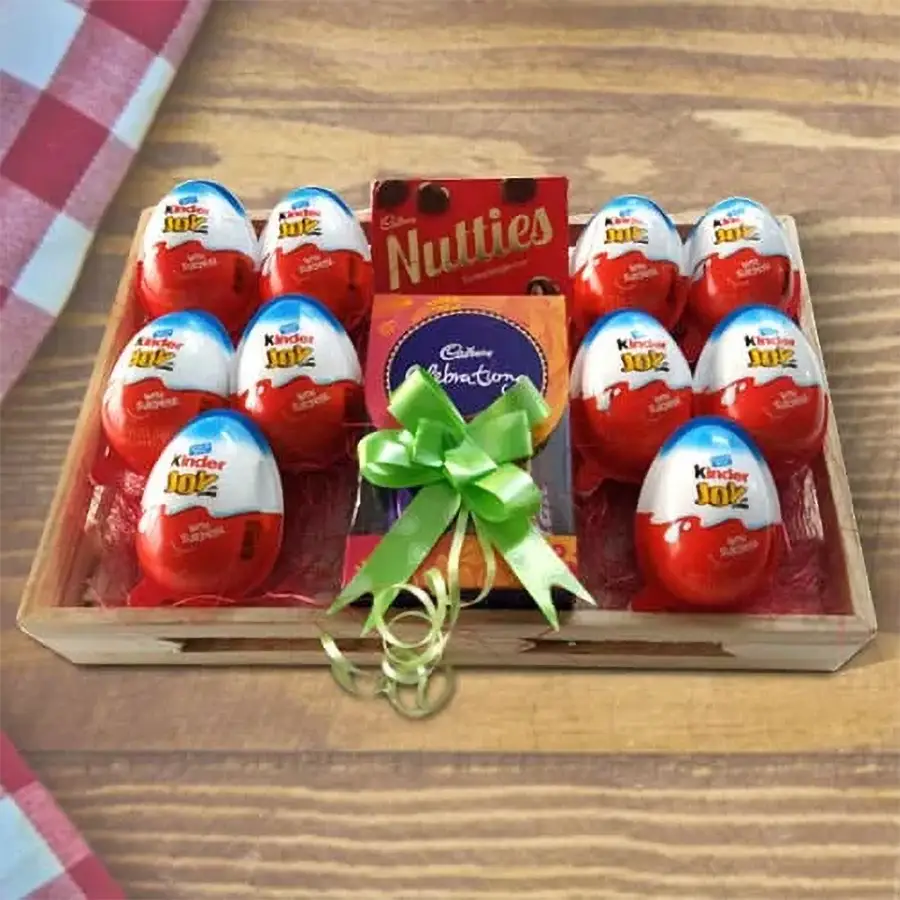 Tray of mixed chocolates for kids featuring Kinder Joy eggs, Cadbury Nutties, and assorted Cadbury chocolates arranged on a wooden tray.