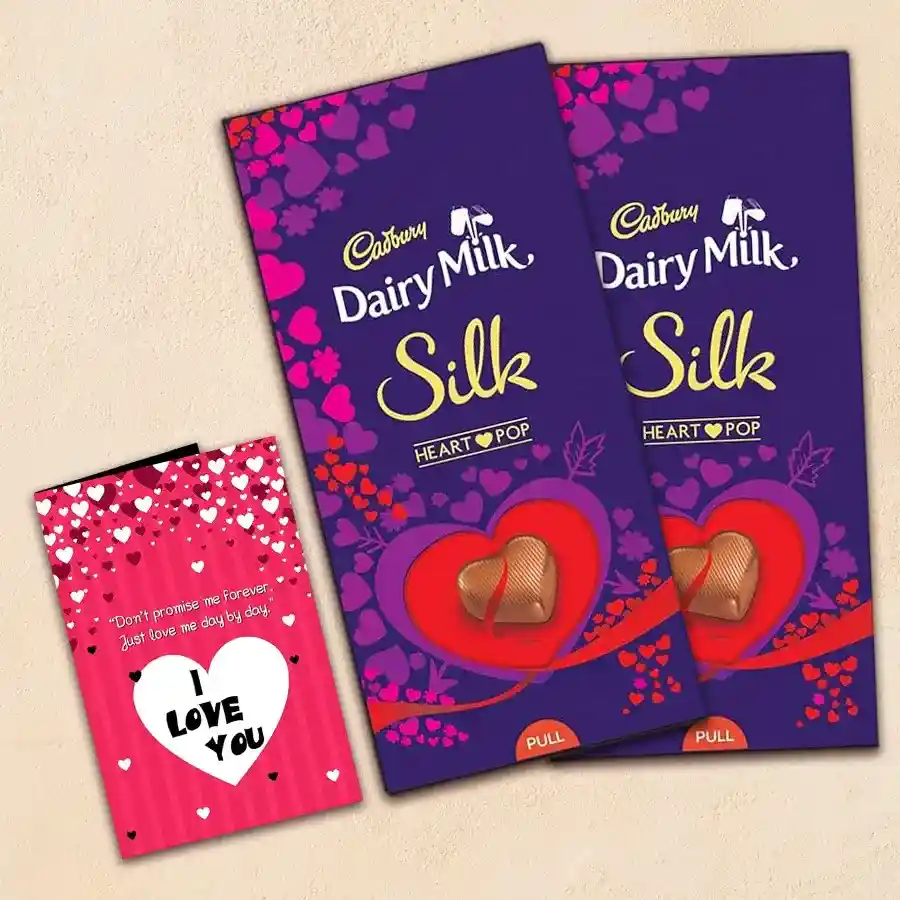 Two Cadbury Dairy Milk Silk Heart Pop-Out bars wrapped for Valentine's Day alongside a Valentine's card.