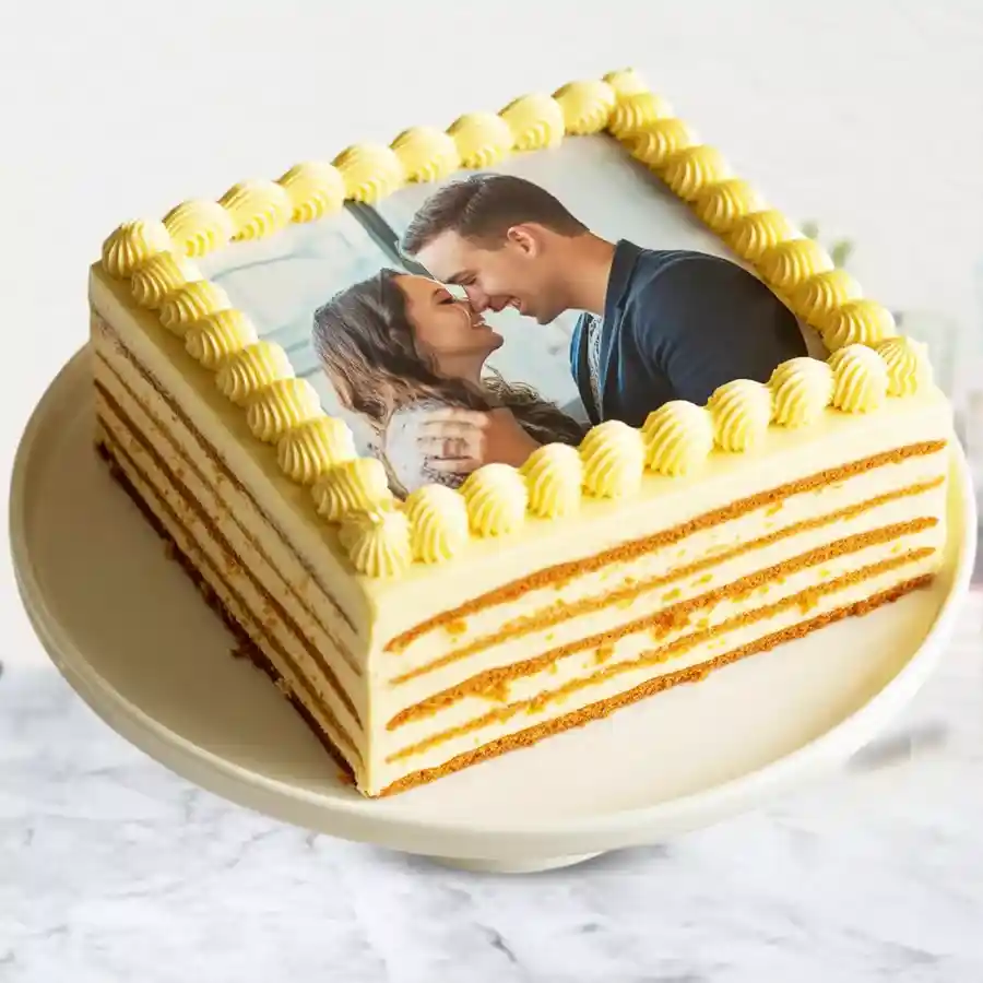 Square vanilla photo cake with white frosting, adorned with chocolate, personalized with custom photo on top.