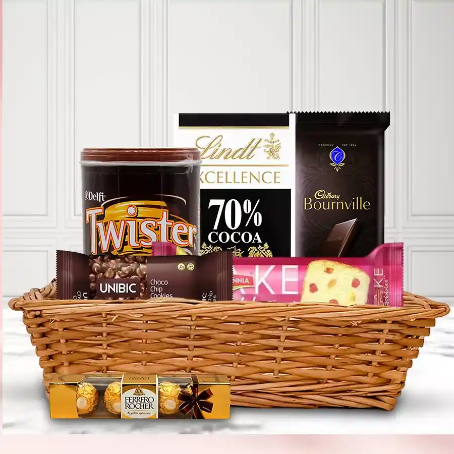 A beautifully arranged chocolate gift basket featuring Britannia Fruits Cake, Cadbury Bournville, Lindt Bar, Twister Chocolate Rolled Wafers, Unibic Choco Chip Cookies, and Ferrero Rocher Minis.