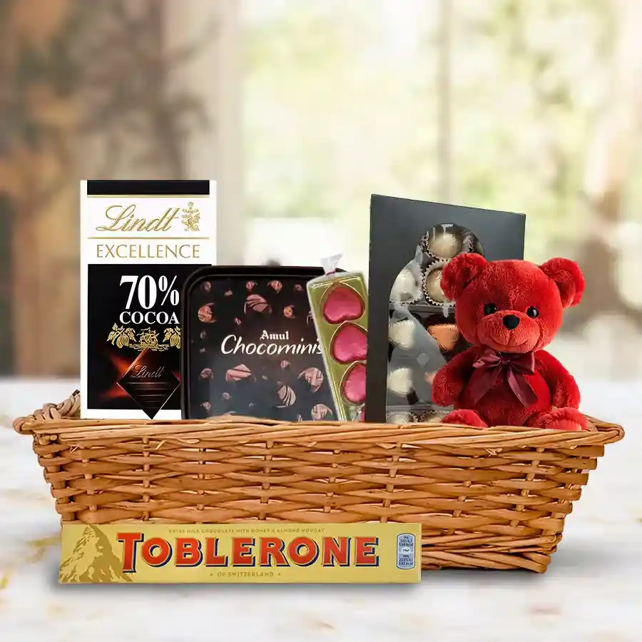 Chocolate gift basket featuring an adorable teddy bear, assorted chocolates, and sweets, beautifully arranged in a small basket.