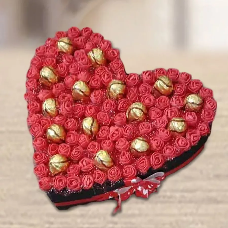 Heart-shaped arrangement of 16 sapphire chocolates on a bed of vibrant artificial roses