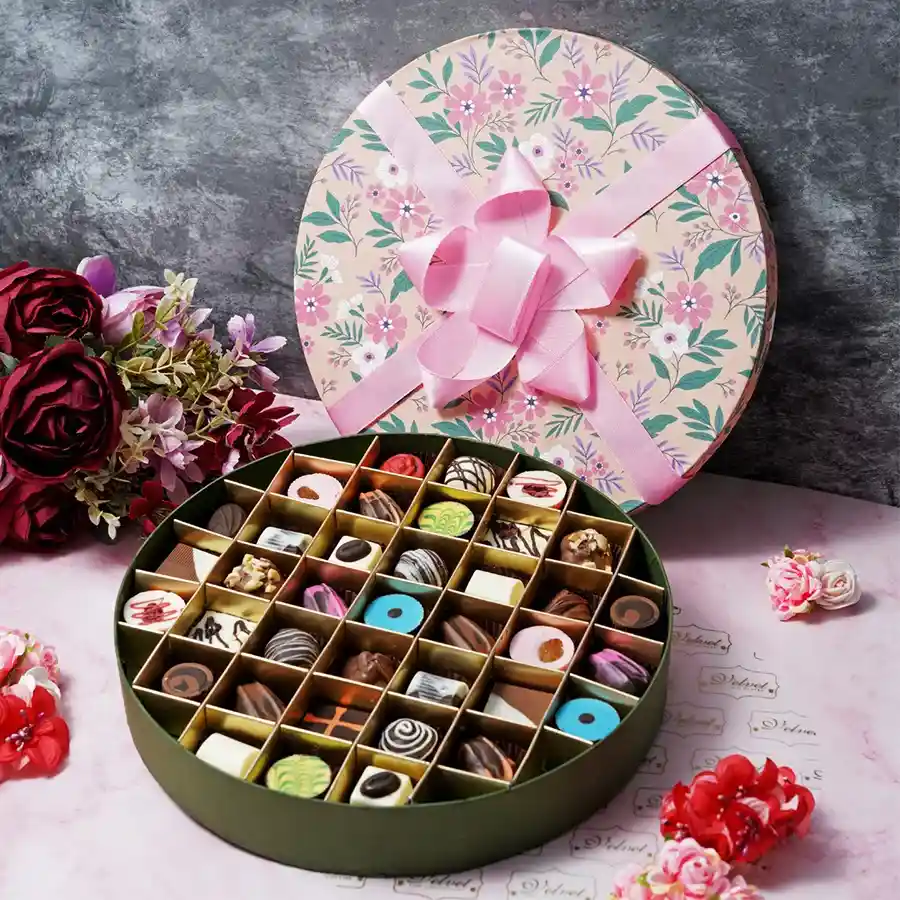 A beautifully arranged round floral box filled with 37 assorted handcrafted chocolates in various flavors including rose, pistachio, orange, cranberry, blueberry, almonds, and hazelnuts, perfect for Mother's Day.