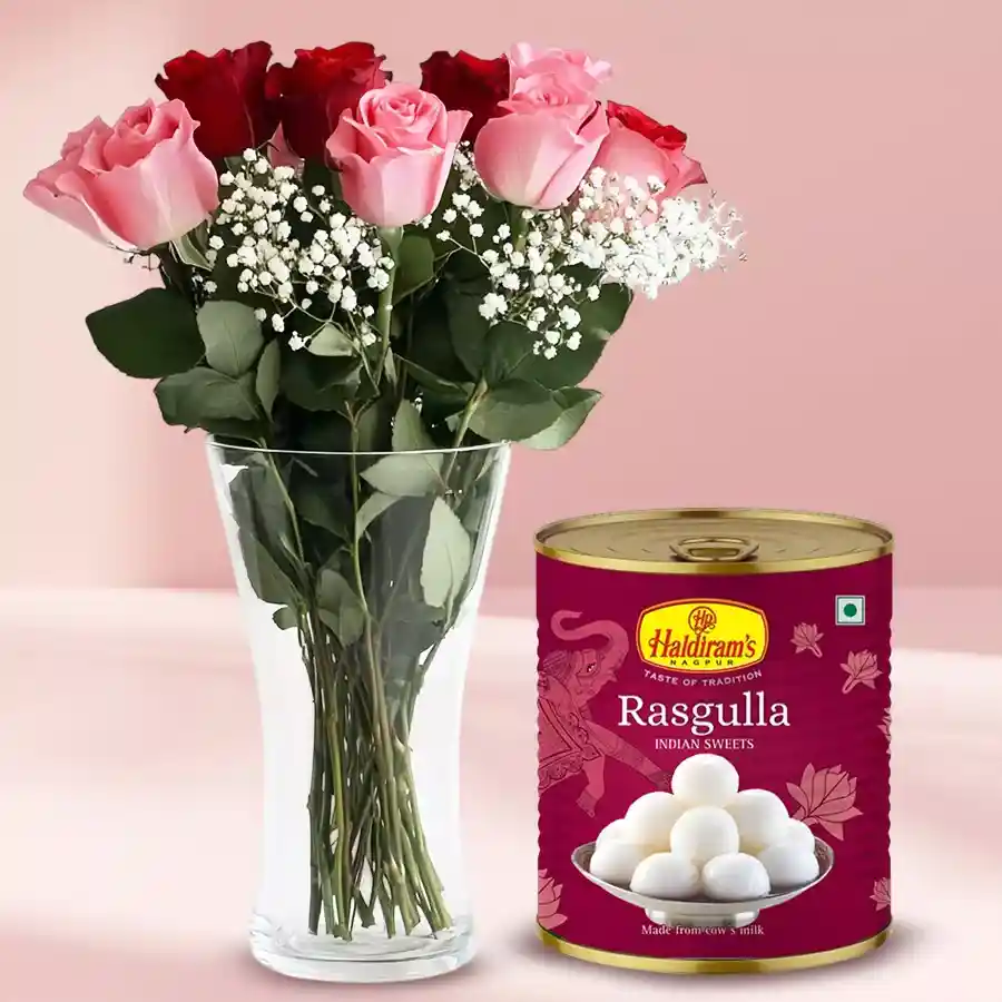 A beautiful glass vase filled with 12 pink and 12 red roses, gypsophila, and green leaves, accompanied by a 1 Kg tin of Haldiram Rasgulla.