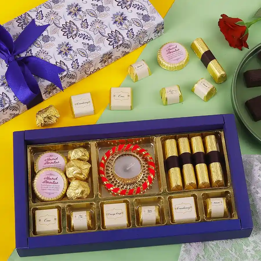 Festive mix of sweet treats including Almond Chocolate Florentines, Almond Chocolate Rocks, Granola Logs, assorted chocolates, and a diya for Diwali celebrations