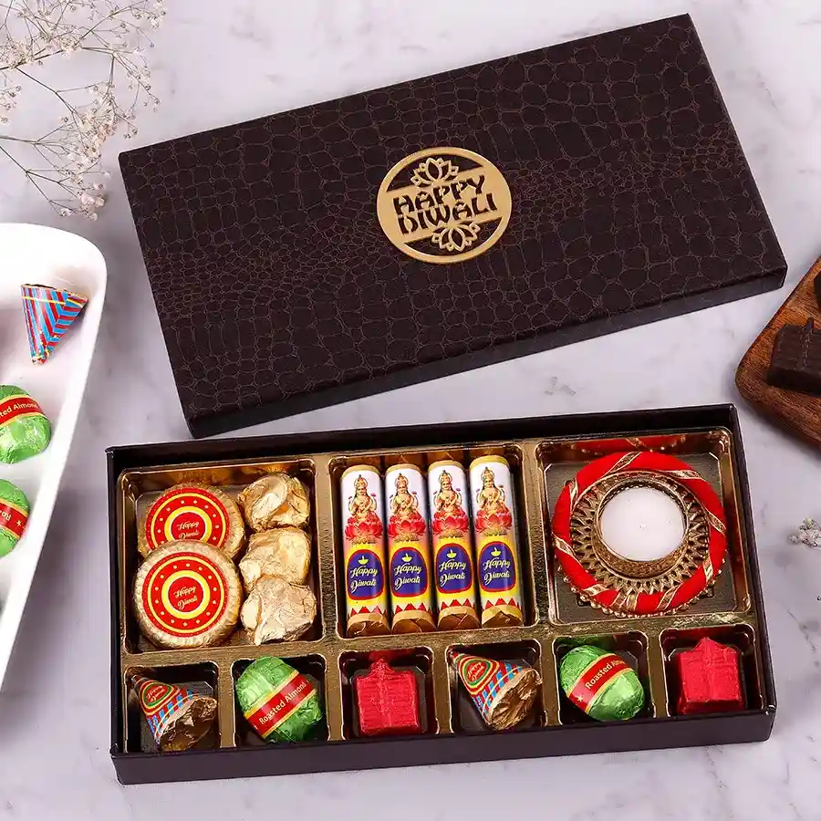A colorful assortment of festive chocolates and firecrackers arranged in a decorative box, featuring almond florence, chocolate rocks, diya-shaped chocolates, and more, symbolizing Diwali celebrations.