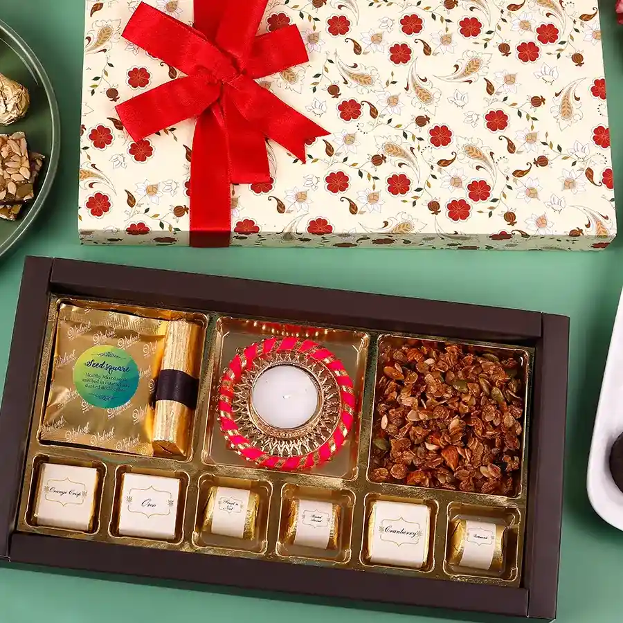 Chocolates N Granola Gift Set featuring a crunchy Seeds Square, Chocolate Granola Log, an edible Diya, 50g of granola, and assorted chocolates in a festive arrangement.