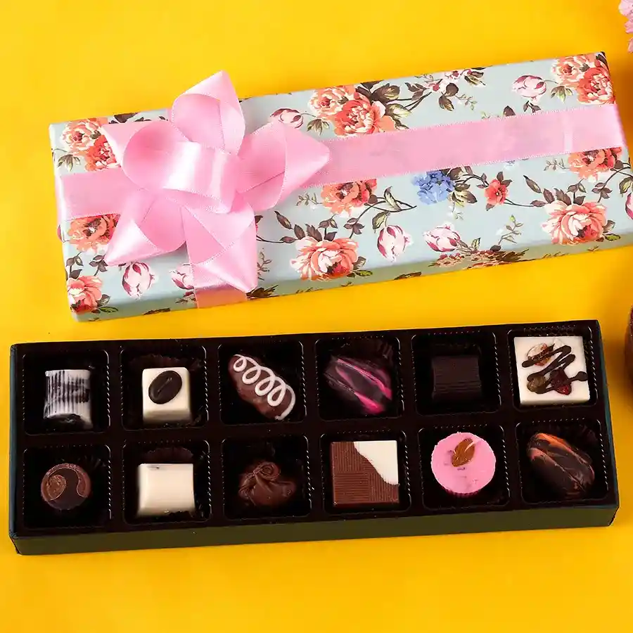 An elegant box containing a variety of 12 assorted chocolates alongside delicate flowers, showcasing a colorful mix of flavors and textures.