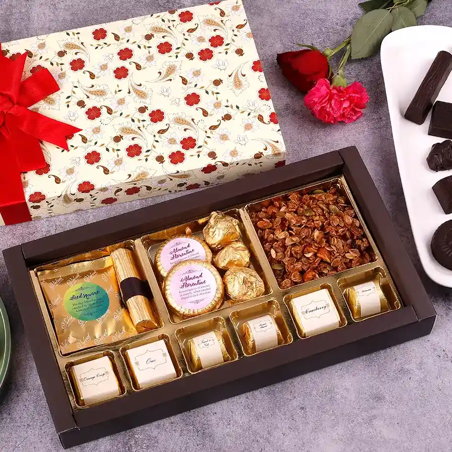 An assortment of chocolates and crunchy snacks including smooth seed chocolate, granola chocolate log, almond florentines, almond rocks, granola, and assorted chocolates like Oreo and butterscotch arranged attractively.