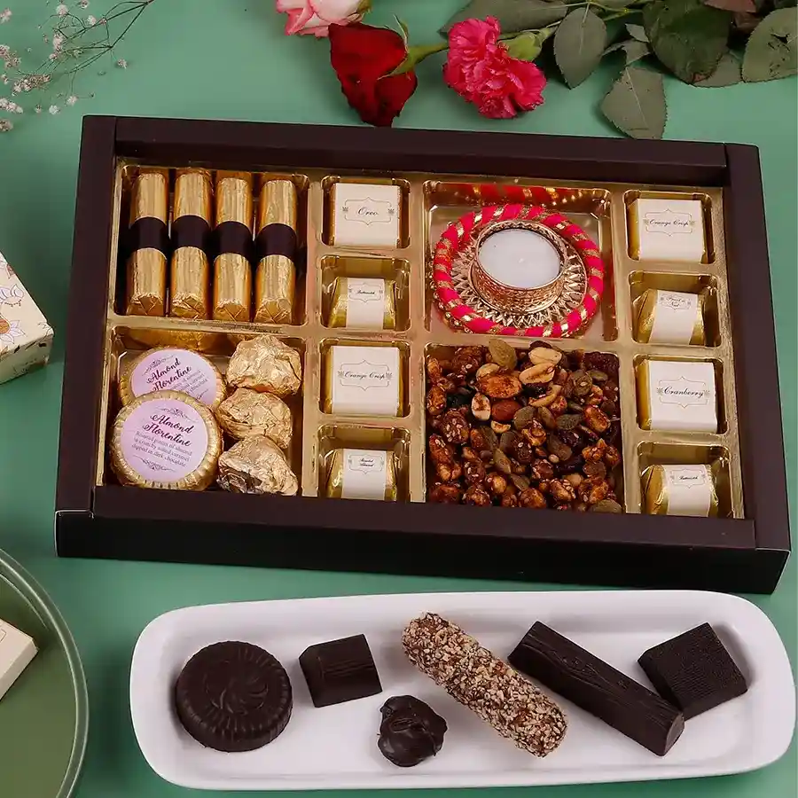 A festive box of Diwalis Delicious Chocolate Medley featuring crunchy granola chocolate logs, almond florentines, almond rocks, assorted chocolates, a sweet and spicy trail mix, and a diya for celebrations.