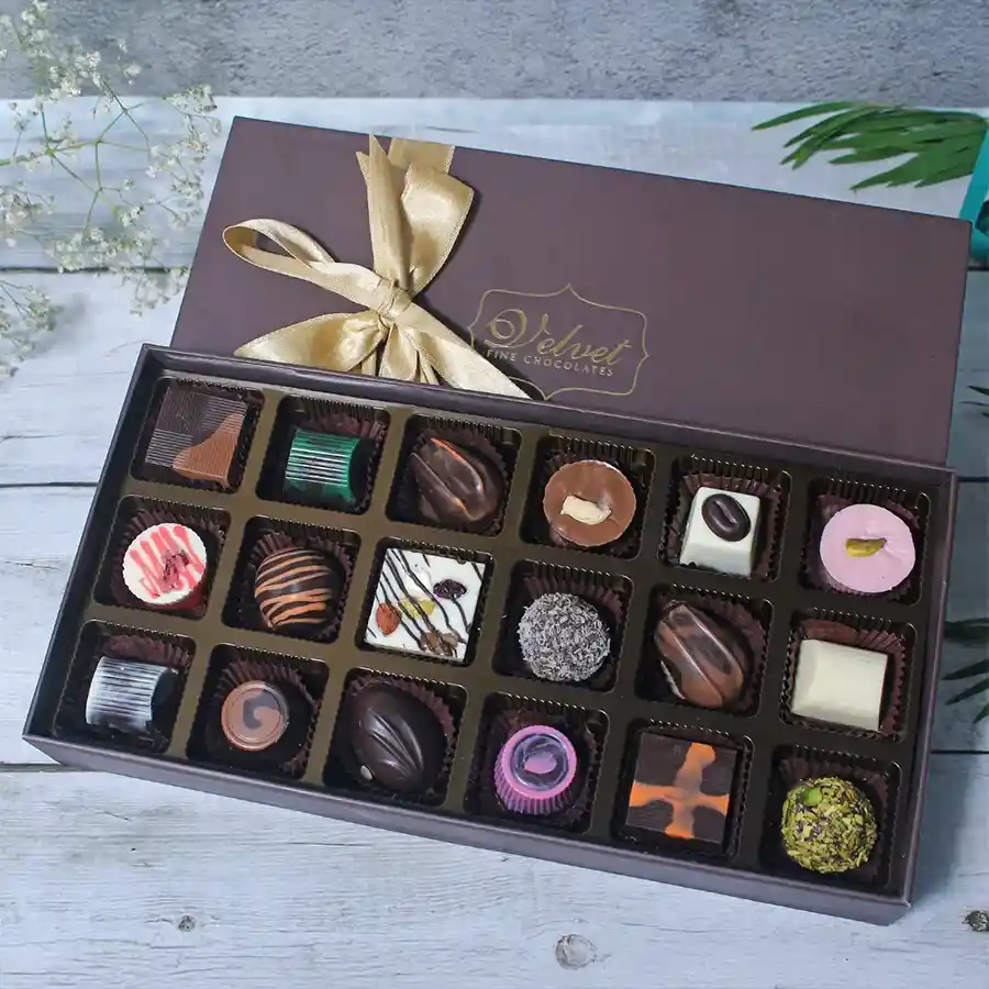A beautifully arranged box of assorted gourmet chocolates including Mocca, Caramel, Orange, Mint, Cranberry, Blueberry, Fruit n Nut, Roasted Almonds, and Orange Crisp, with festive decorations.