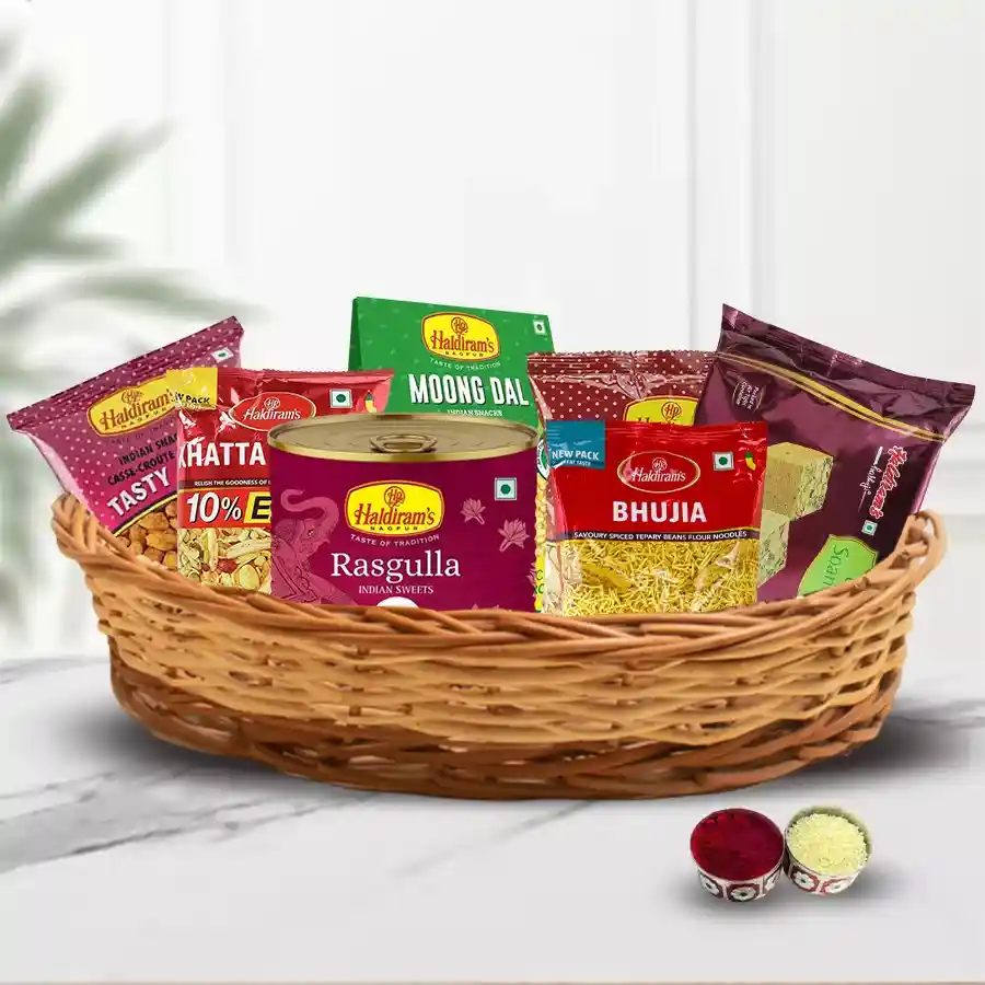Ecstatic Haldirams Sweets N Snacks Basket featuring Badam Pakodi, Soan Papdi, Rasgulla, Bhujia, and decorative Roli, Tilak, and Chawal for Bhai Dooj celebration.