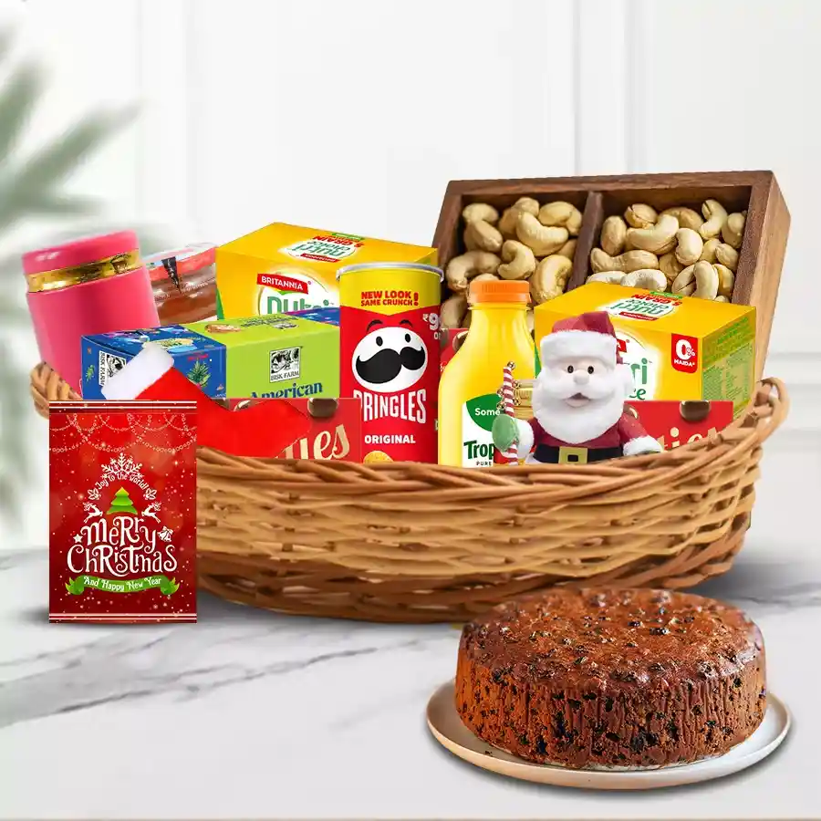 A beautifully arranged Christmas delicacy basket filled with festive treats including fruit cake, biscuits, Pringles, orange juice, marmalade, assorted cookies, dry fruits, honey, a Santa soft toy, festive stockings, and a Christmas card.