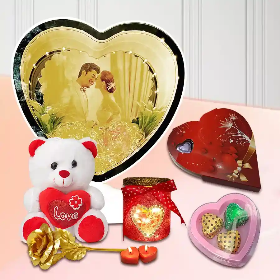 Charismatic Valentine Day Gift Hamper featuring a personalized photo heart magic mirror, heart-shaped candles, a teddy bear, a golden rose, a heart LED lamp, heart-shaped chocolates, and a festive tin box with assorted handmade treats.