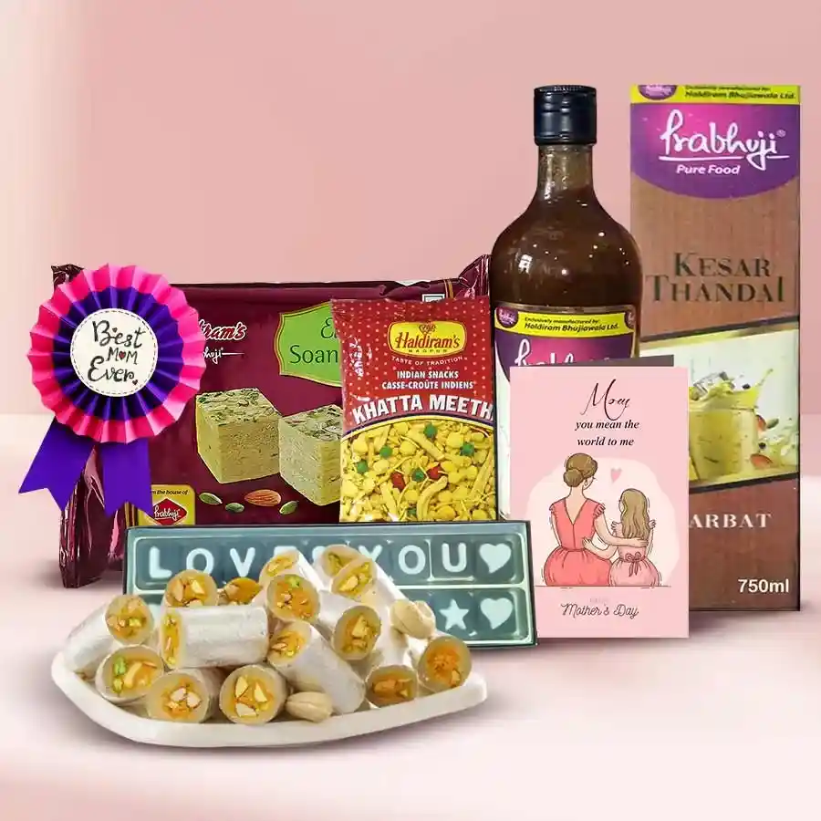 Gift hamper filled with treats for Mother's Day, including Haldirams Soan Papdi, Kaju Rolls, Khata Meetha, chocolates, Thandai Syrup, a Mother's Day card, and a Best Mother Award badge.