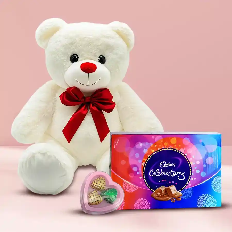 Big White Teddy bear with a red bow beside a heart-shaped red tin filled with handmade chocolates and a box of Cadbury Celebrations.