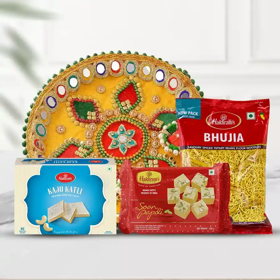 Gift from Haldirams package featuring a Pooja Thali, Kaju Katli, Soan Papdi, and Bhujia arranged beautifully.