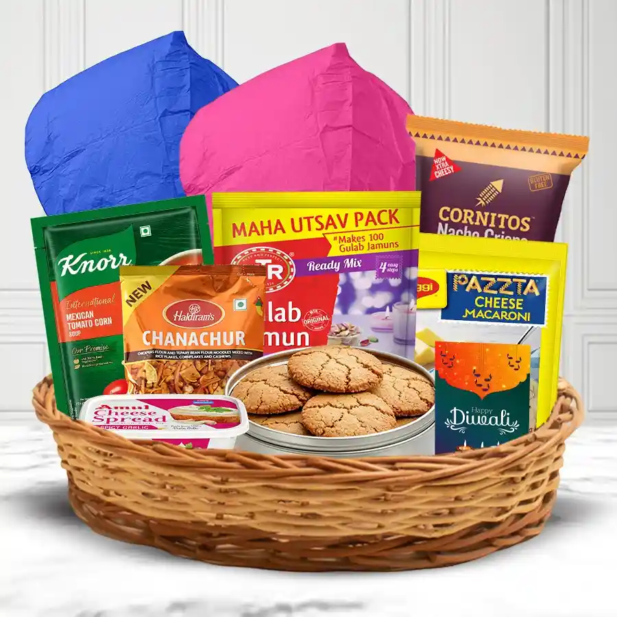 A beautifully arranged Diwali gifts hamper featuring ginger cookies, nachos, cheese dip, macaroni, soup mix, gulab jamun mix, snacks, flying lanterns, and a greetings card in a reusable cane basket.