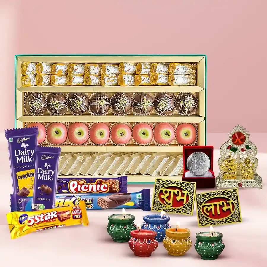 A beautifully arranged gift hamper featuring assorted Indian sweets, rich Cadbury chocolates, decorative items including mud diyas, a Ganesh Laxmi Mandap, Subh Labh wall stickers, and a silver-plated Ganesh Laxmi coin.
