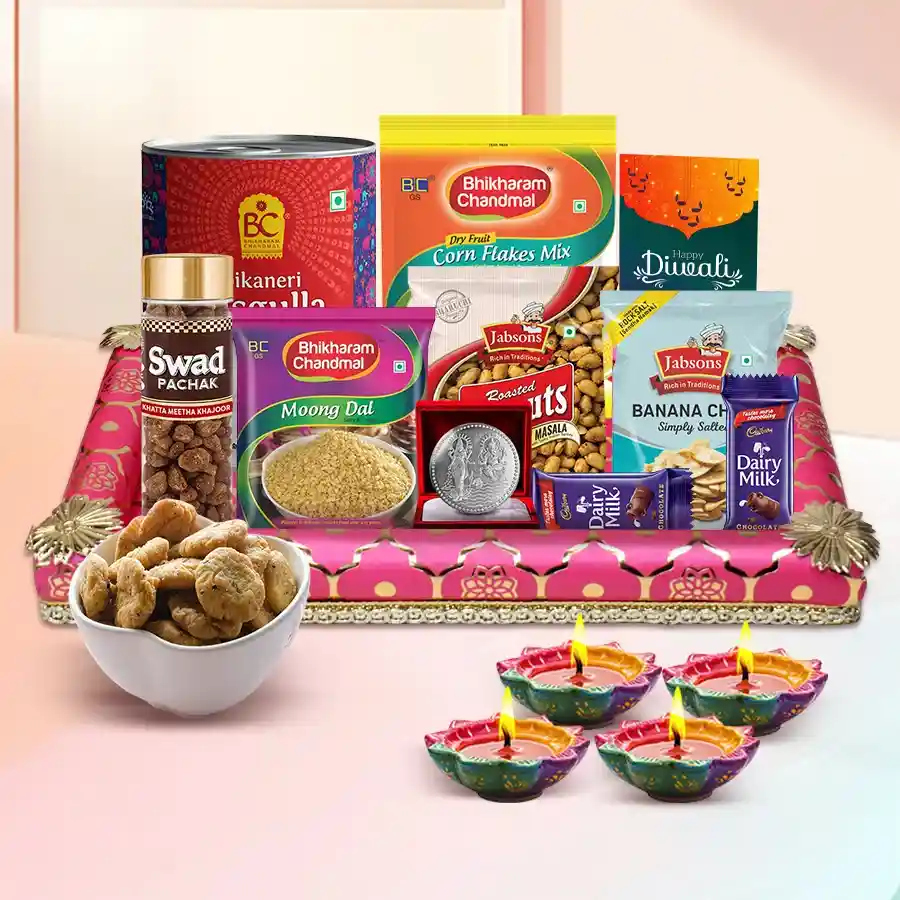 A vibrant Diwali snacks hamper filled with Jabson roasted peanuts, banana chips, Bhikaram’s cornflakes mix, dalmoth, swali, rasgollas, Cadbury Dairy Milk chocolates, decorated diyas, a beautiful tray, and a silver-plated Ganesh-Laxmi coin, along with a Diwali greetings card.