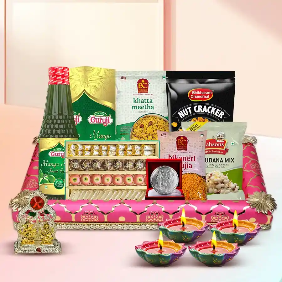A festive gift hamper for Diwali featuring traditional sweets, snacks, designer diyas, a Ganesh Laxmi Mandap, a silver-plated coin, and a decorated tray.