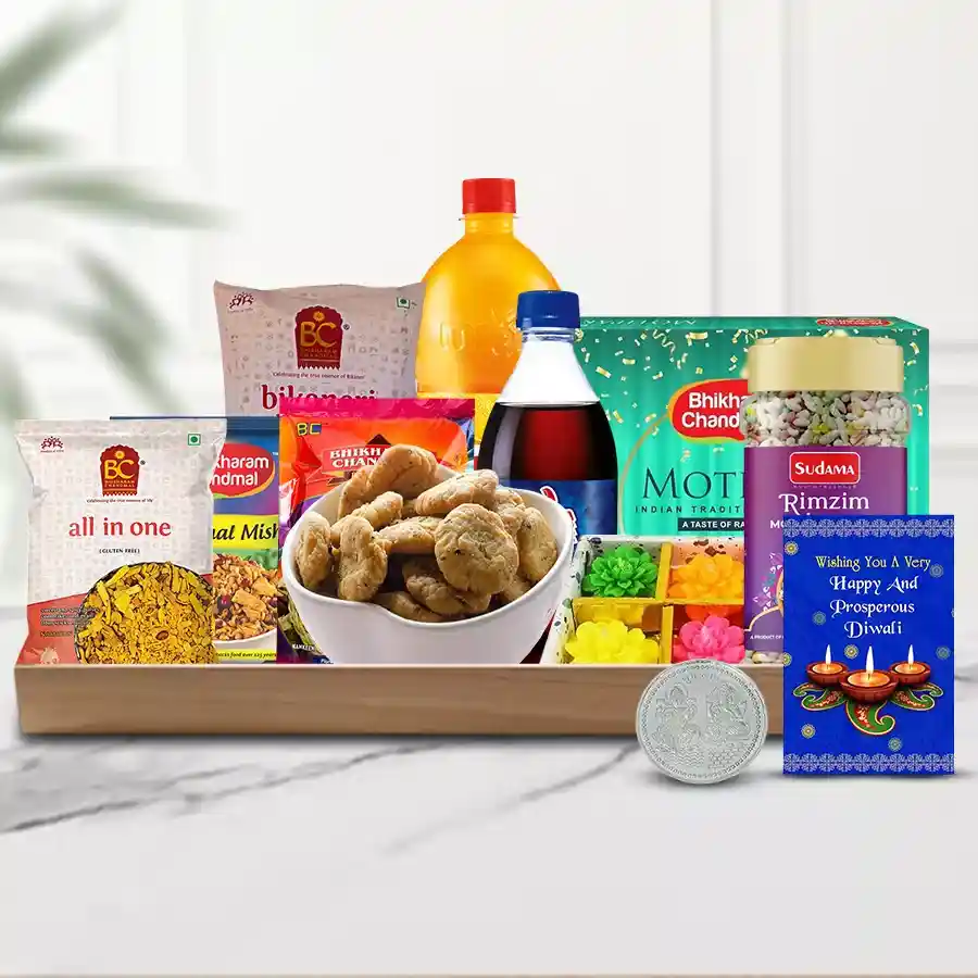 A beautifully arranged Diwali gift hamper featuring sweets, snacks, drinks, decorative candles, a greeting card, a Ganesh-Laxmi coin, and a reusable tray.