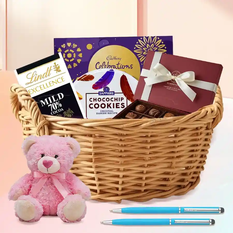 Exclusive Chocos n Assortments Gift Hamper featuring Lindt Excellence and Cadbury Celebration bars, homemade chocolates, Sapphire Cookies, a teddy bear, ballpoint pens, and a cane basket