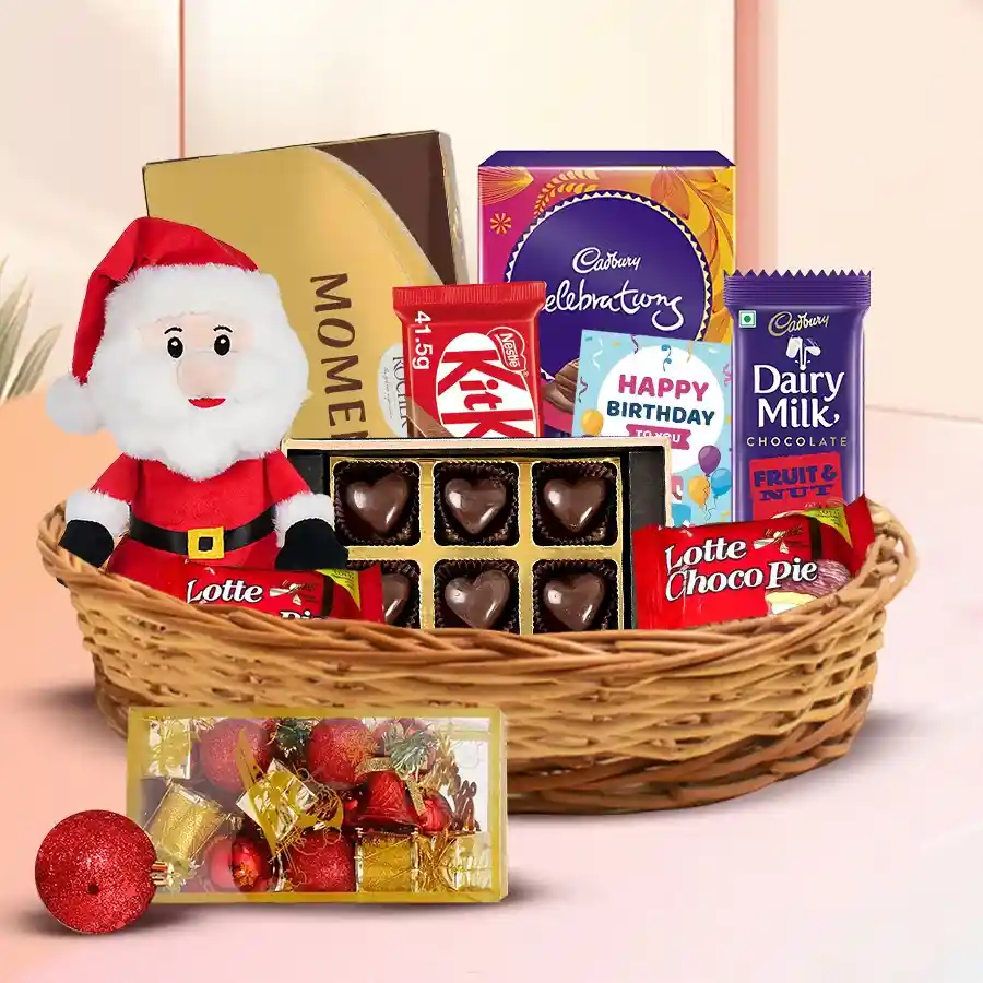 A beautifully arranged Christmas gift hamper filled with chocolates, including Cadbury Mini Celebrations, Ferrero Rocher Moments, Lotte Chocopie, handmade pineapple chocolates, Dairy Milk Fruit & Nut, KitKat, and a festive Santa Claus decoration in a stylish cane basket.