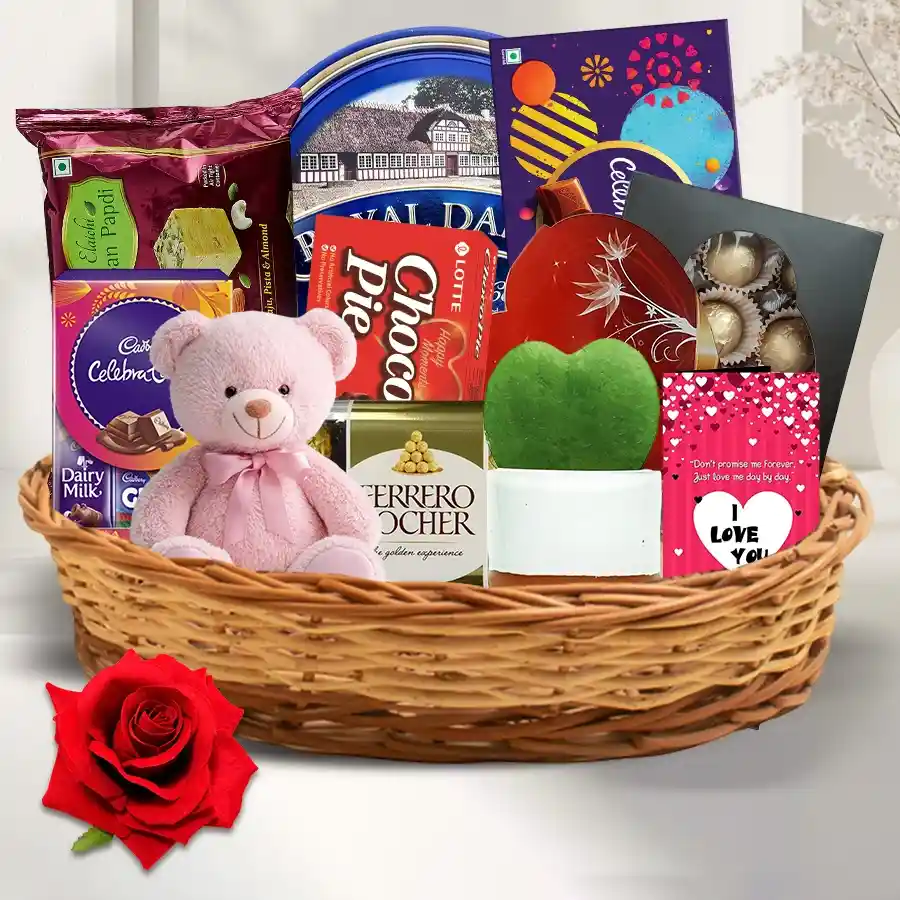 Indulgent Chocolate Delicacies Gift Hamper featuring an assortment of chocolates, Danish Butter Cookies, Soan Papdi, Chocopie, a red velvet rose, a 6-inch teddy bear, a Heart Shaped Leaf plant, and a "I love You" card.