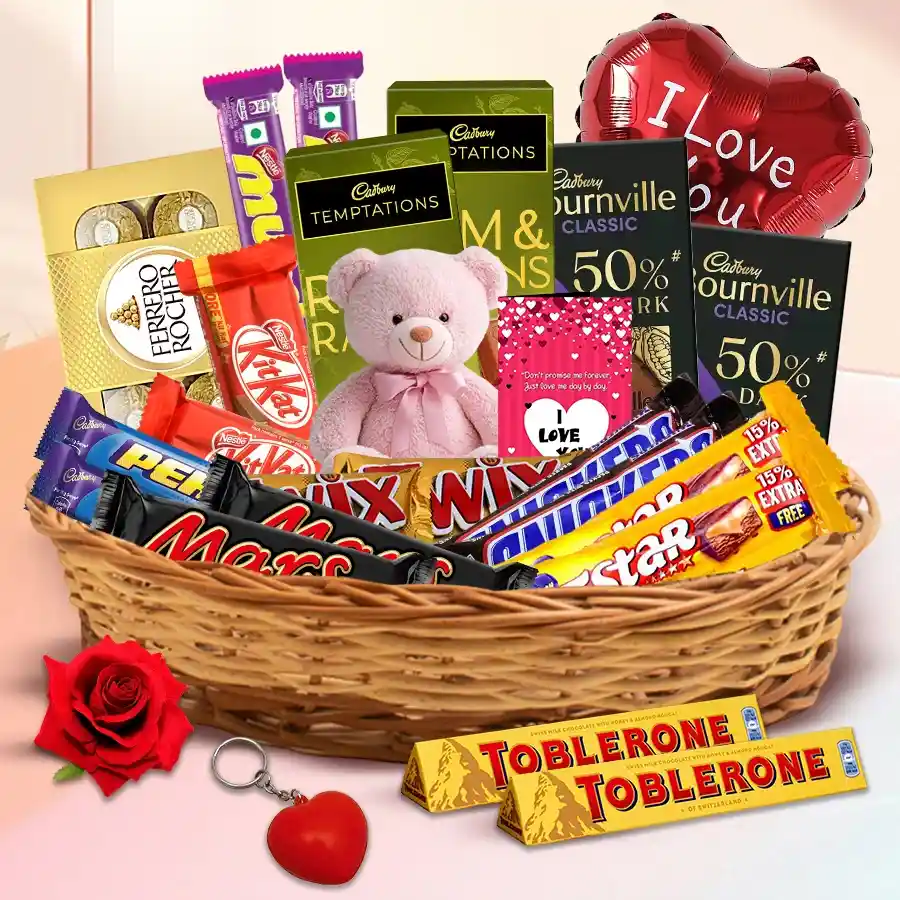 Assorted chocolates gift basket with Valentine accessories including a teddy bear, rose, key ring, card, and balloon.