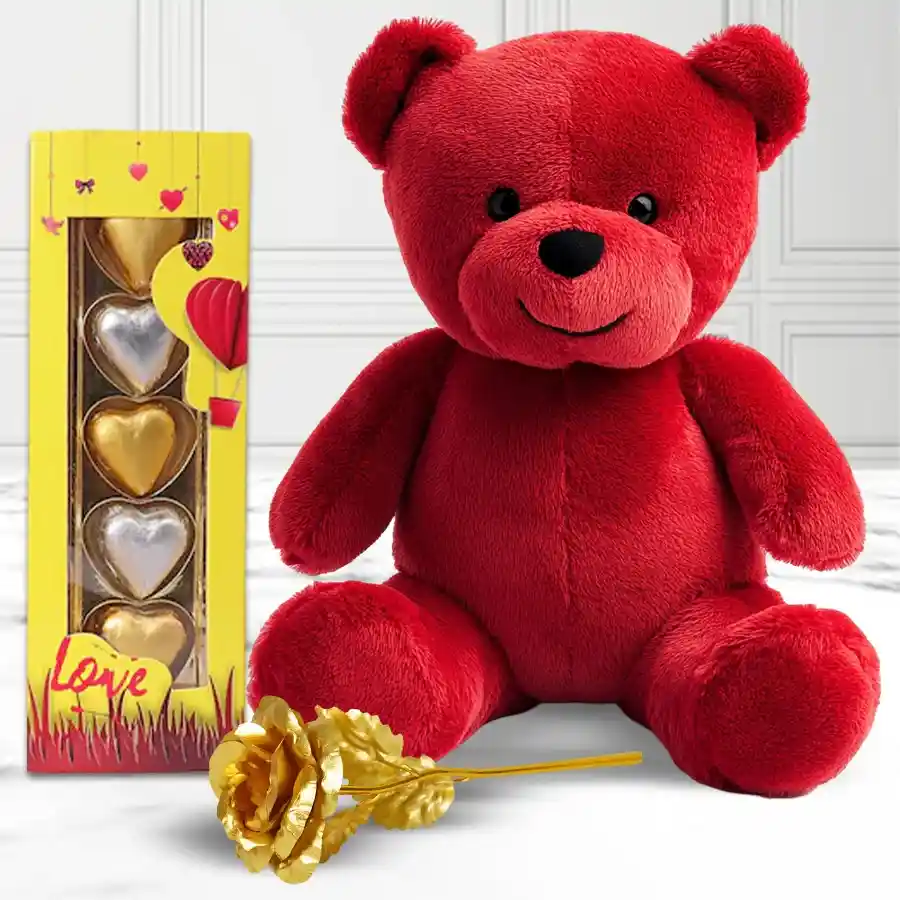 Soft red teddy bear holding a heart alongside five golden heart chocolates and a golden rose in an elegant gift set for Valentine's Day.