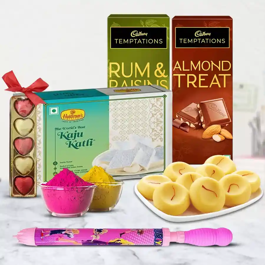 A colorful assortment of Festival of Colors gift items including Haldirams Kaju Katli, Kesaria Peda, Cadbury Temptation bars, homemade chocolates, a Pichkari water cannon, and herbal gulal, all beautifully packaged.