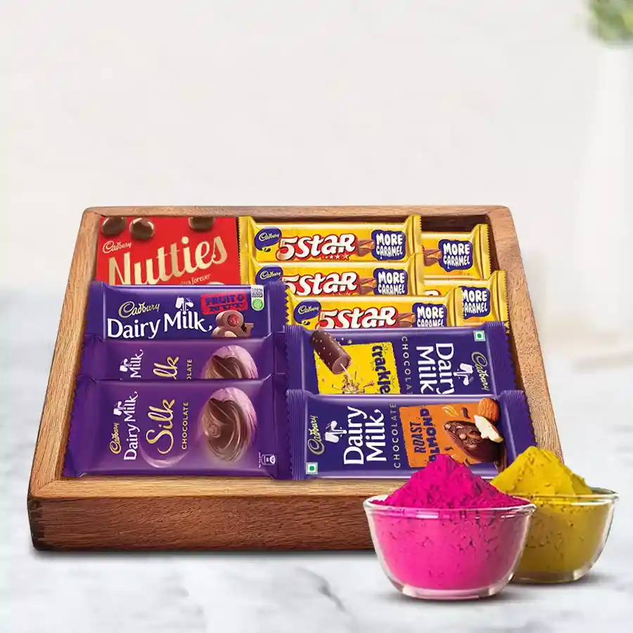 Sumptuous mixed chocolates gift tray featuring Cadbury classics like Dairy Milk Silk and Fruit n Nut, elegantly arranged on a wooden tray with vibrant herbal gulal for Holi celebrations.