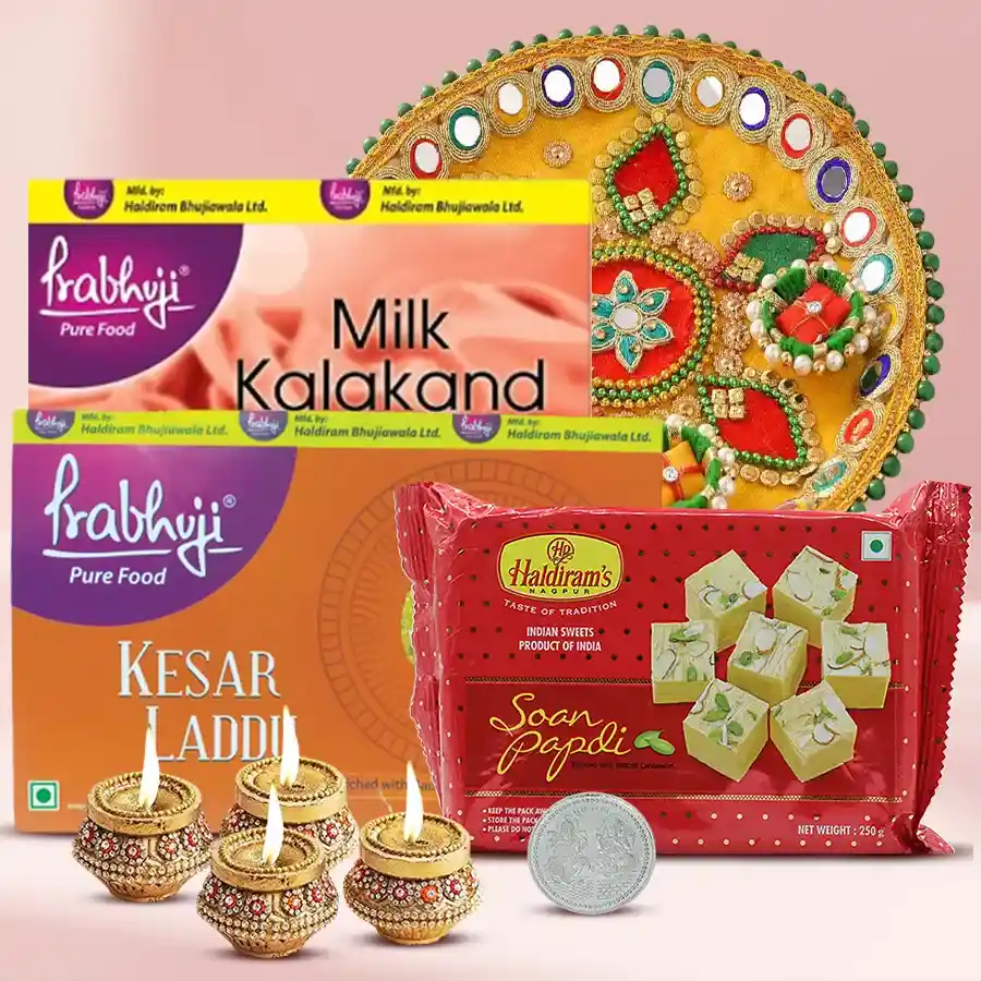 Ambrosial Haldiram Gift Hamper featuring Milk Kalakand, Kesaar Laddu, Soan Papdi, Designer Steel Thali, terracotta Diyas, and Laxmi Ganesh Silver Plated Coin for Diwali celebrations.