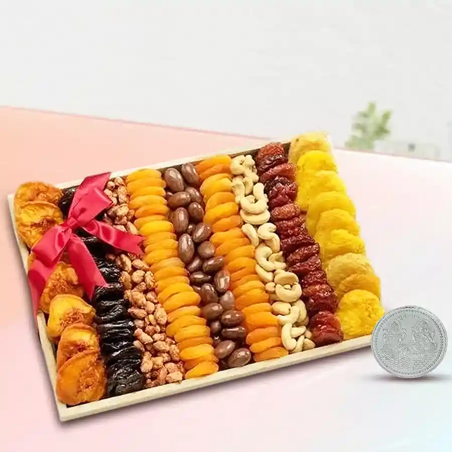 A festive gift hamper featuring dry fruits like dried prunes, apricots, cashews, a silver plated Laxmi Ganesh coin, and a wooden tray, beautifully arranged for Diwali celebration.