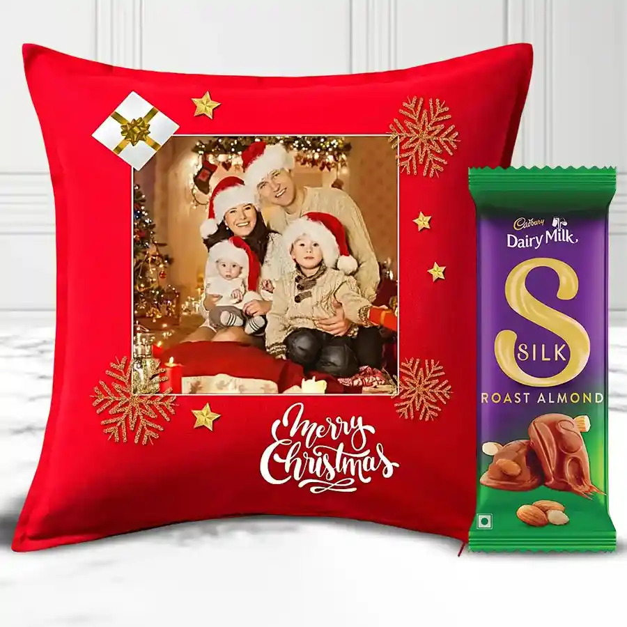 Personalized pink Merry Christmas fur cushion with a heart shape and a Cadbury Dairy Milk Silk Roast Almond Chocolate Bar on a festive background.