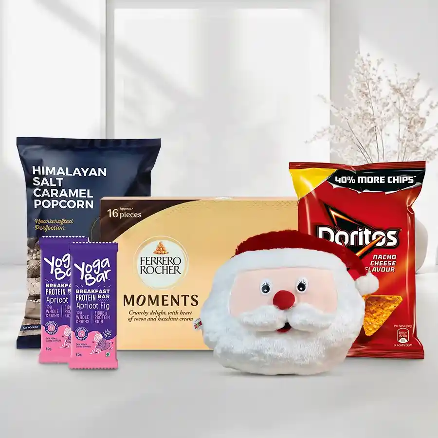 Colorful holiday gift set for kids featuring a Santa Claus cushion, Yoga protein bars, Doritos, Himalayan Salt Caramel popcorn, and Ferrero Rocher chocolates.