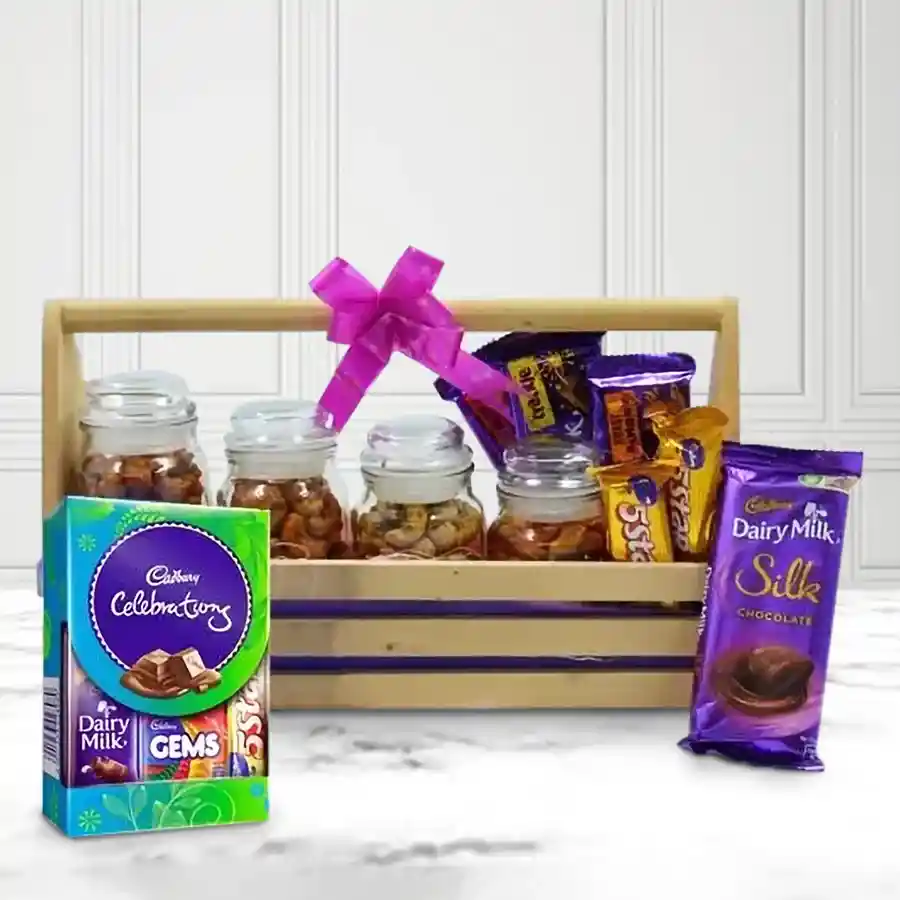 A wooden tray filled with flavored cashews in Cheese, Peryperry, Pizza, and Barbecue varieties, alongside an assortment of Cadbury chocolates including Celebrations, Dairy Milk Silk Hazelnut, Crackle, Fruit & Nut, Roast Almond bars, and 5 Star bars.