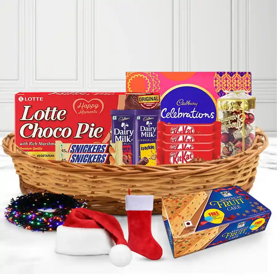 Heavenly Christmas Cake Chocolate and Décor Combo in a stylish cane basket featuring American Fruit Cake, Cadbury treats, KitKats, Snickers, Christmas decorations, twinkling lights, caps, and stockings.