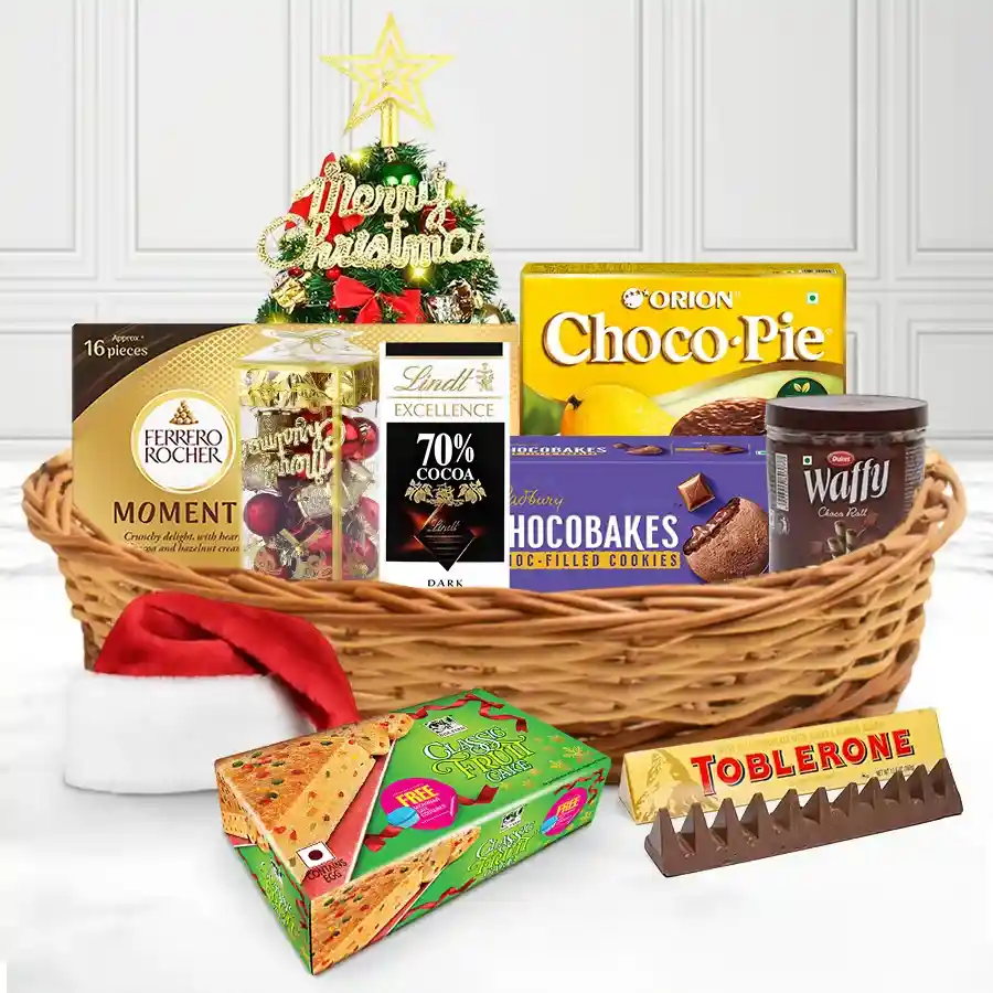 A festive basket filled with various chocolates and treats, decorated with Christmas ornaments and topped with a tree cap.