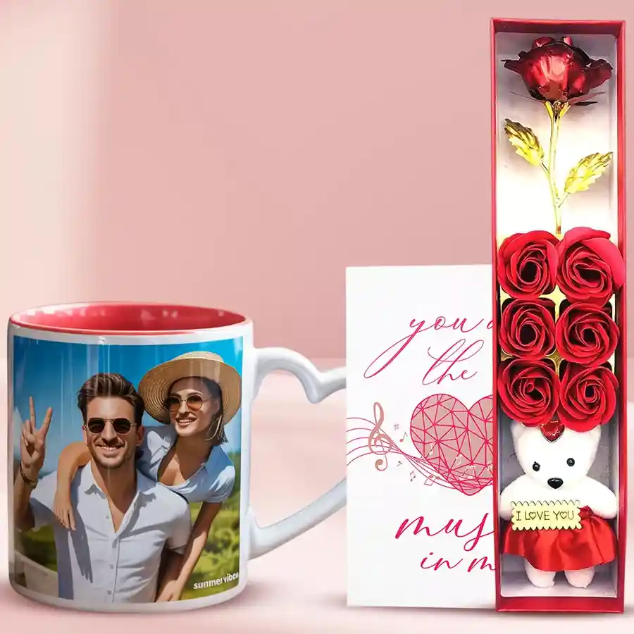 Lovely trio of artificial red roses, a personalized heart-handle coffee mug, a cuddly teddy bear, and a musical Valentine's greeting card arranged together, conveying a romantic gift theme.