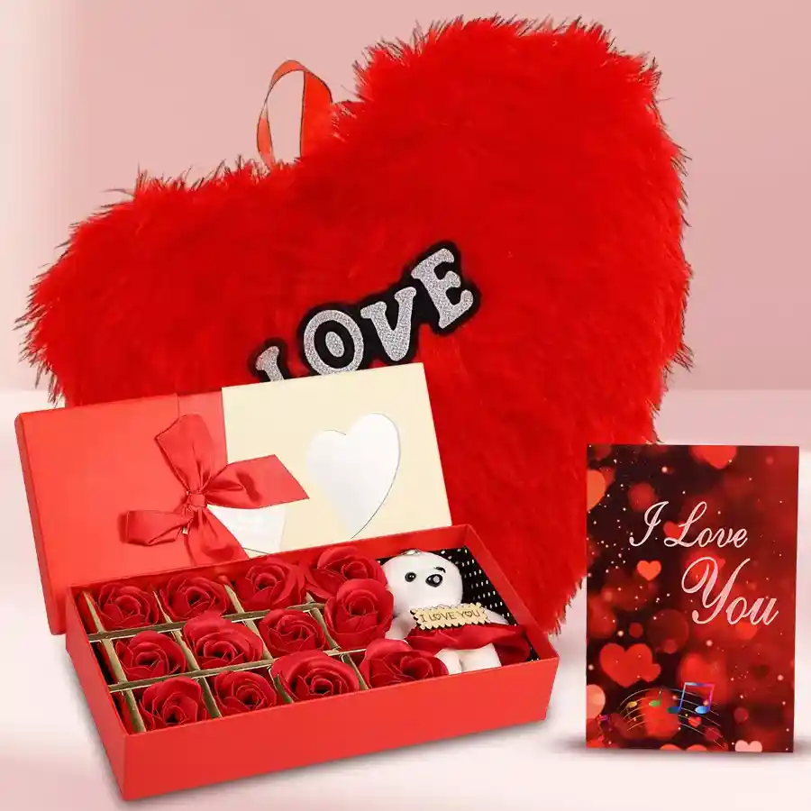 An Exclusive Teddy surrounded by Artificial Red Roses, a heart-shaped cushion, and a musical greeting card on display.
