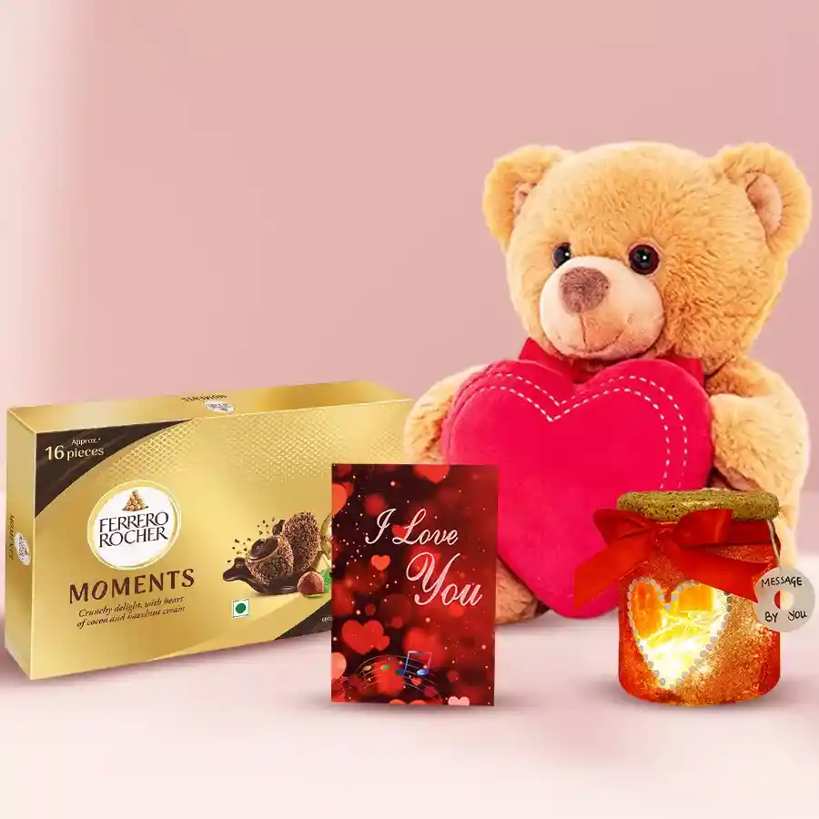 A curated Valentine's gift pack featuring a brown teddy bear with a heart, a box of Ferrero Rocher Moments chocolates, an LED Lightning Lamp Jar, and a Musical Valentine Card.