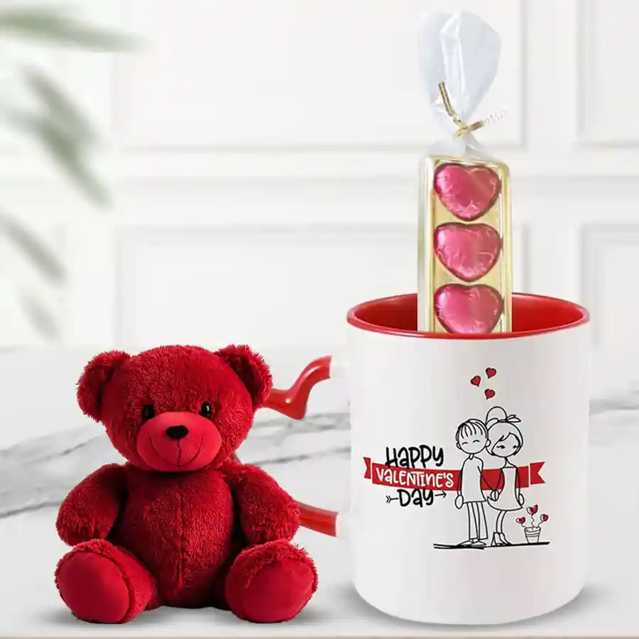 A red teddy bear, a printed coffee mug with a heart handle, and a pack of five heart-shaped handmade chocolates arranged together for Valentine's Day.