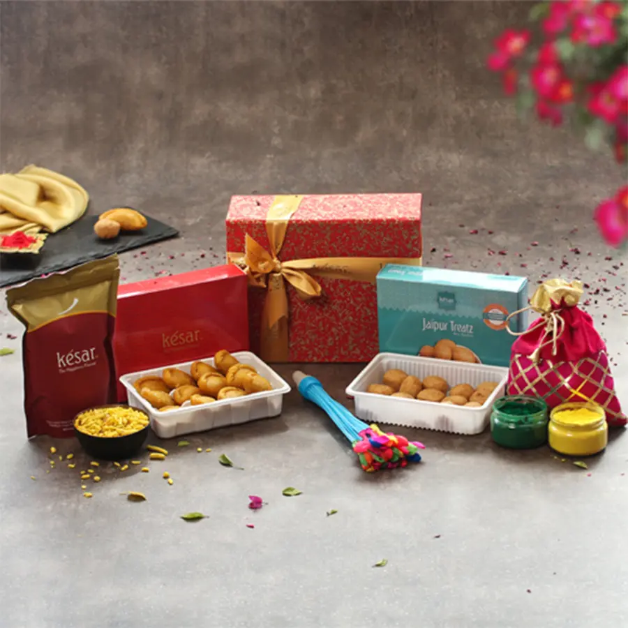 Assorted Holi hamper featuring Kesar Gujiya, Mini Kachori, Navaratna Mix, a Holi Balti, Pichkari, herbal colors, and a water balloon in a handmade paper box with a greeting card